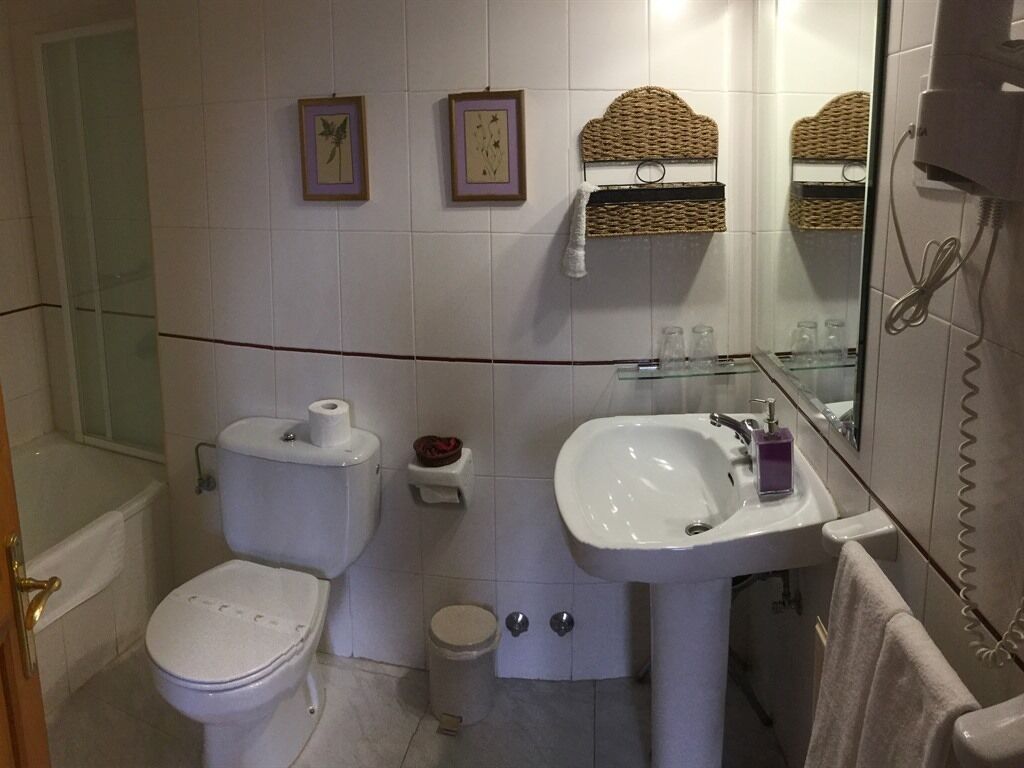 Un baño con inodoro, lavamanos y cabina de ducha de vidrio. Hay dos cuadros enmarcados en la pared, un perchero y una cesta sobre el lavamanos.