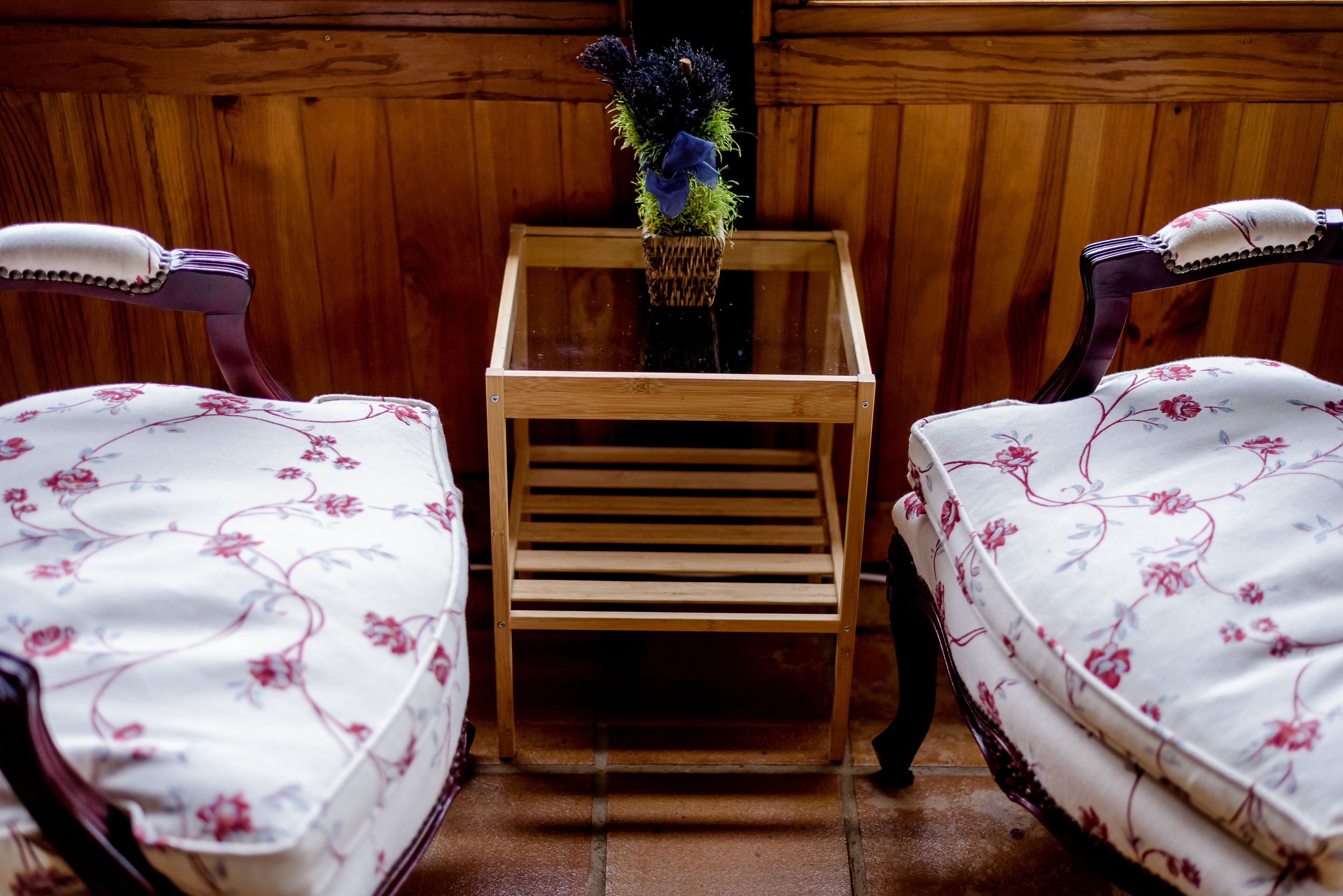 A wooden table with a woven basket containing a floral arrangement, flanked by two upholstered chairs with floral upholstery.