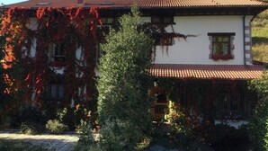 A two-story house with a red-tiled roof, ivy-covered walls, and a mountain backdrop. - Hotel Rural Picos de Europa (Posada de Valdeon)