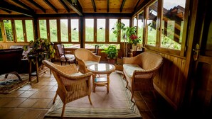 A wooden-paneled room with wicker furniture, large windows, and potted plants. - Hotel Rural Picos de Europa (Posada de Valdeon)
