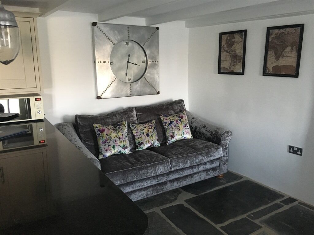 Un salon avec un canapé gris, une grande horloge murale et deux tableaux encadrés.
