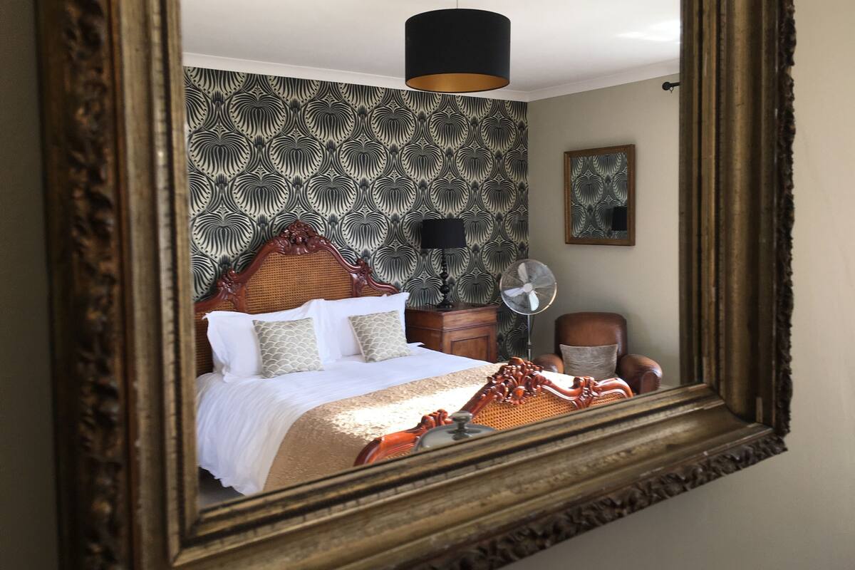 Une chambre à coucher avec un lit, un ventilateur, une chaise et un miroir.