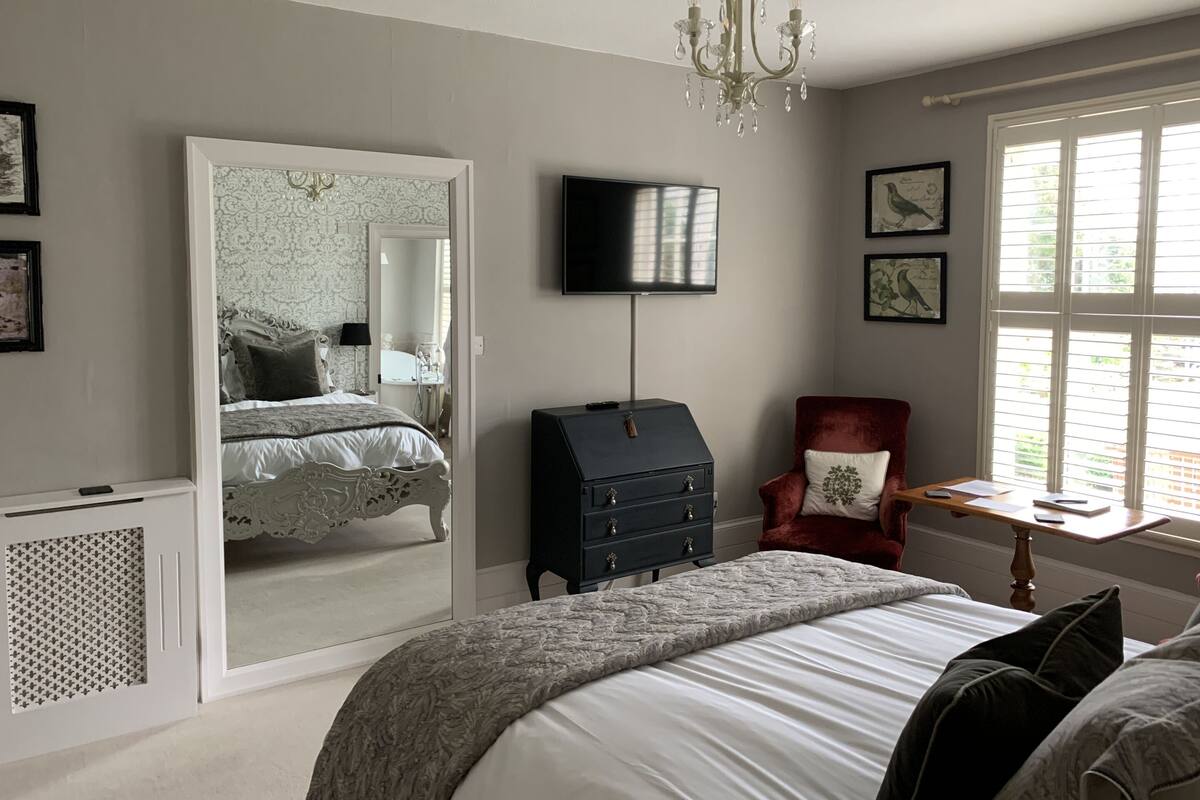 Une chambre à coucher comprenant un lit, une commode, une chaise, un téléviseur et un grand miroir.