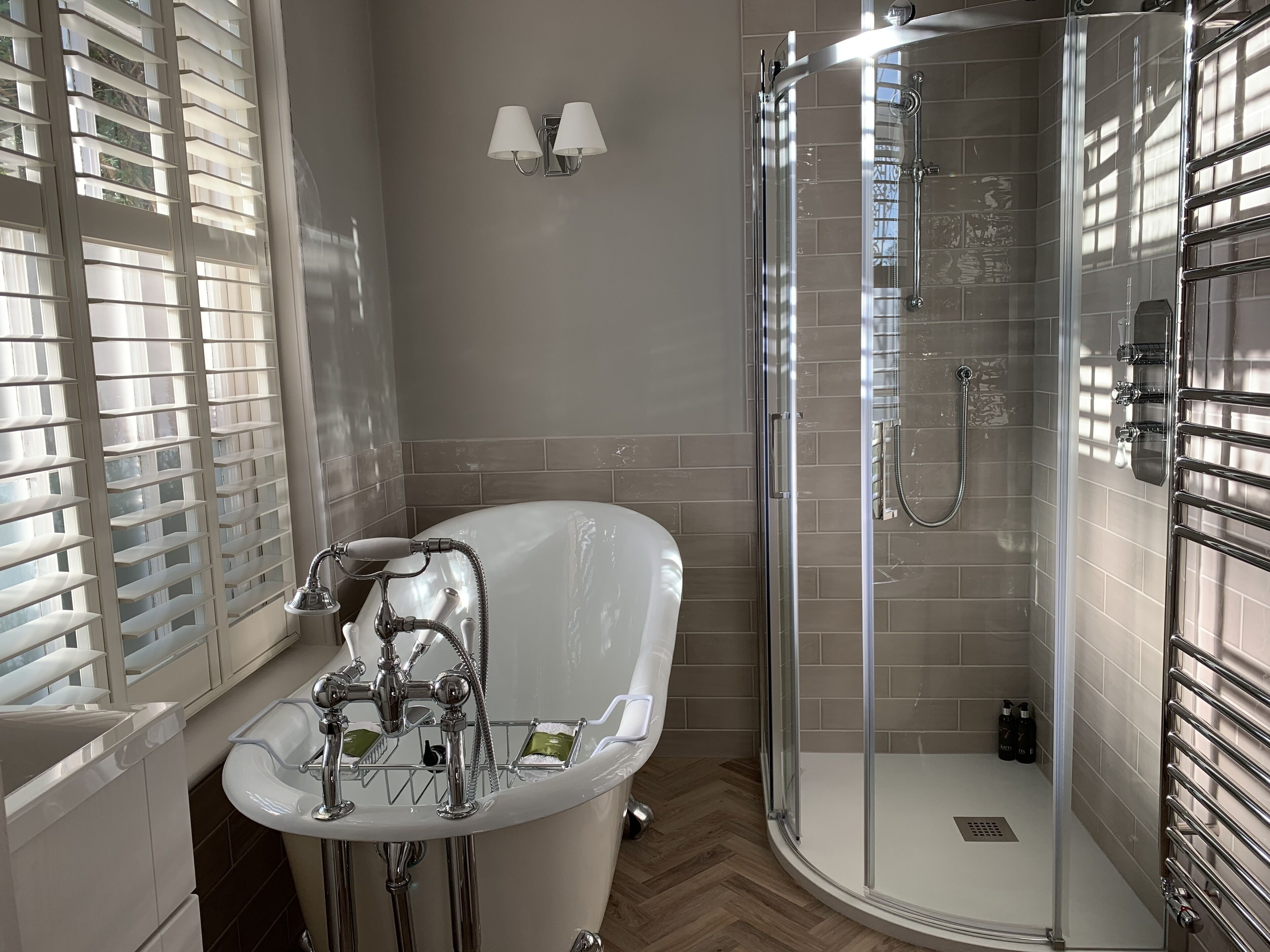 A bathroom with a freestanding bathtub, a glass-enclosed shower, and a window with blinds.