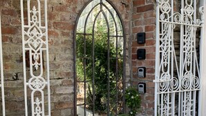 Una silla de mimbre blanca, una reja de hierro forjado y un muro de ladrillo con una ventana.