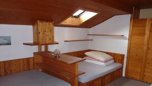 Una petita cabana de fusta amb dos llits superposats, un òcul i un armari de fusta.