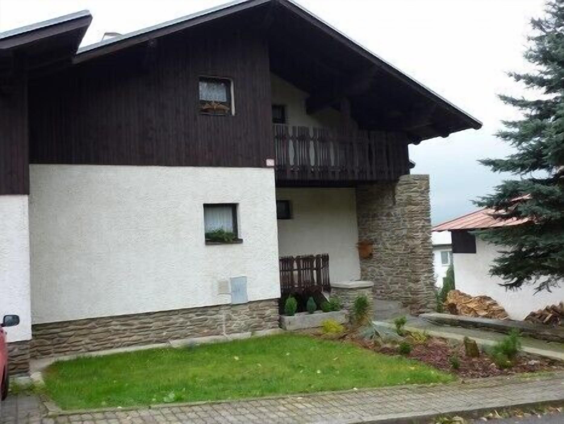 A two-story house with a stone foundation, a balcony, and a small front yard.