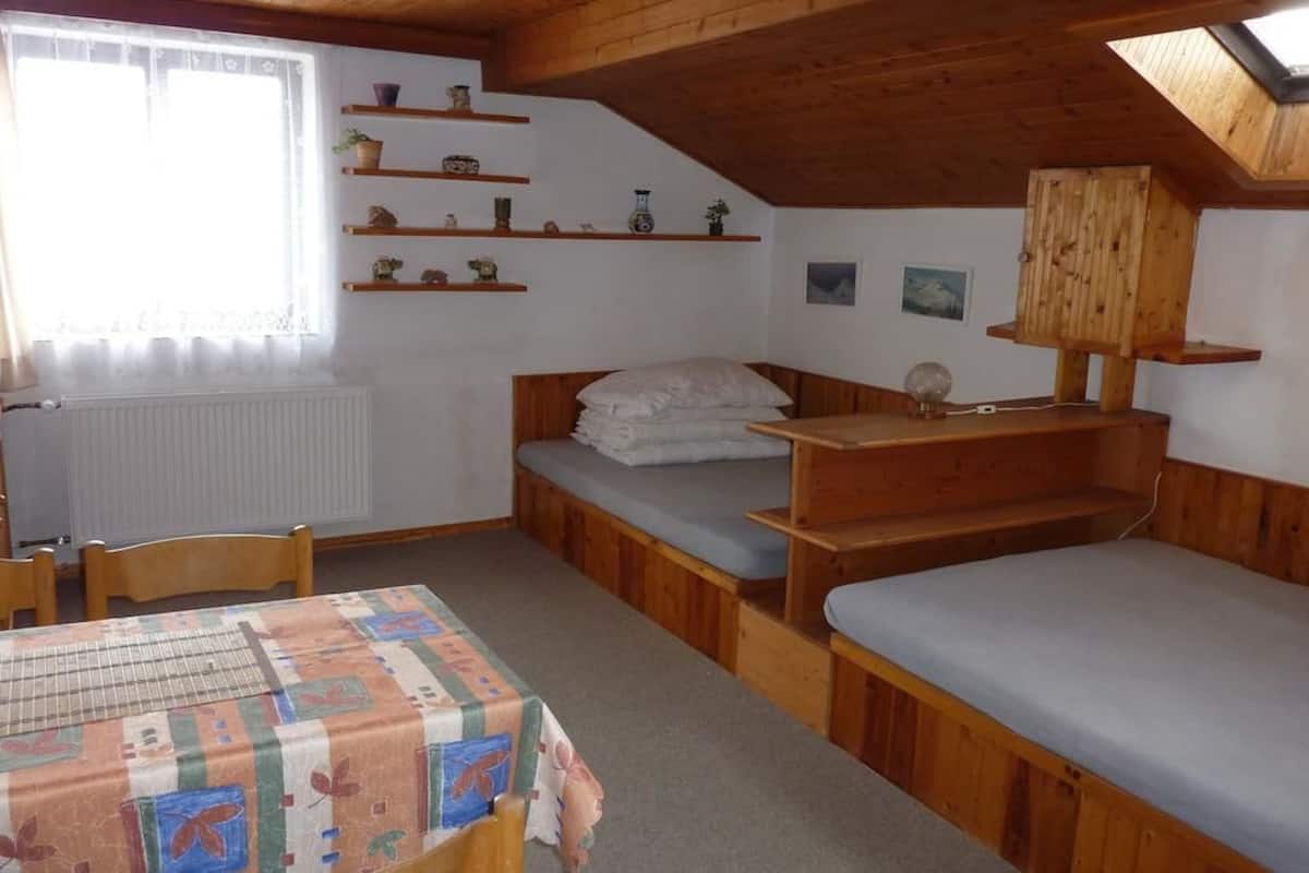 Una habitación pequeña con techo de madera, una cama individual, una mesa con mantel estampado y un radiador.