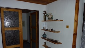 Un passadís amb prestatgeries de fusta que mostren objectes decoratius, una porta de fusta amb panells de vidre gravat i un paviment de rajola.