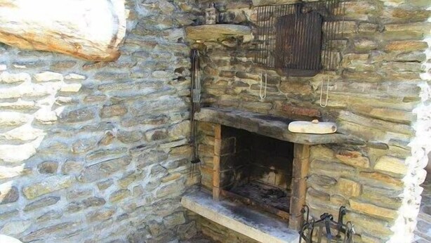 Una llar de pedra encès, una paret de pedra i una prestatgeria de fusta a sobre.