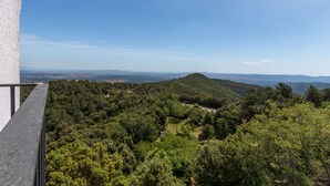 Een balkon met uitzicht op een bebost glooiend landschap en verre bergen.