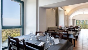 Een restaurant met gedekte tafels, een uitzicht op groen en een hoge plafond.