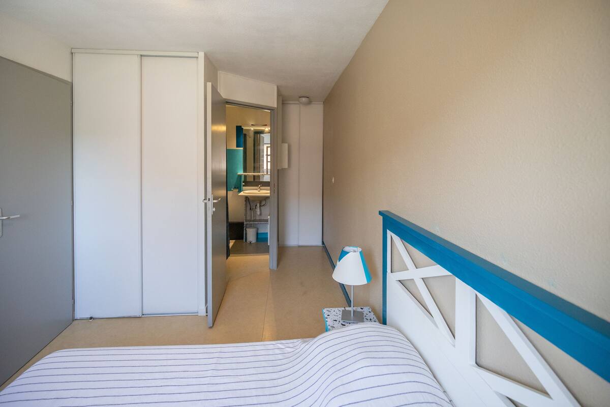 A bedroom with a bed, a nightstand, a lamp, and a door leading to a bathroom.