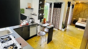 A modern kitchen with a gas stove, a dining area with a table and chairs, and a living area with a sofa and a TV. - 8 Plus Motels (Negombo)