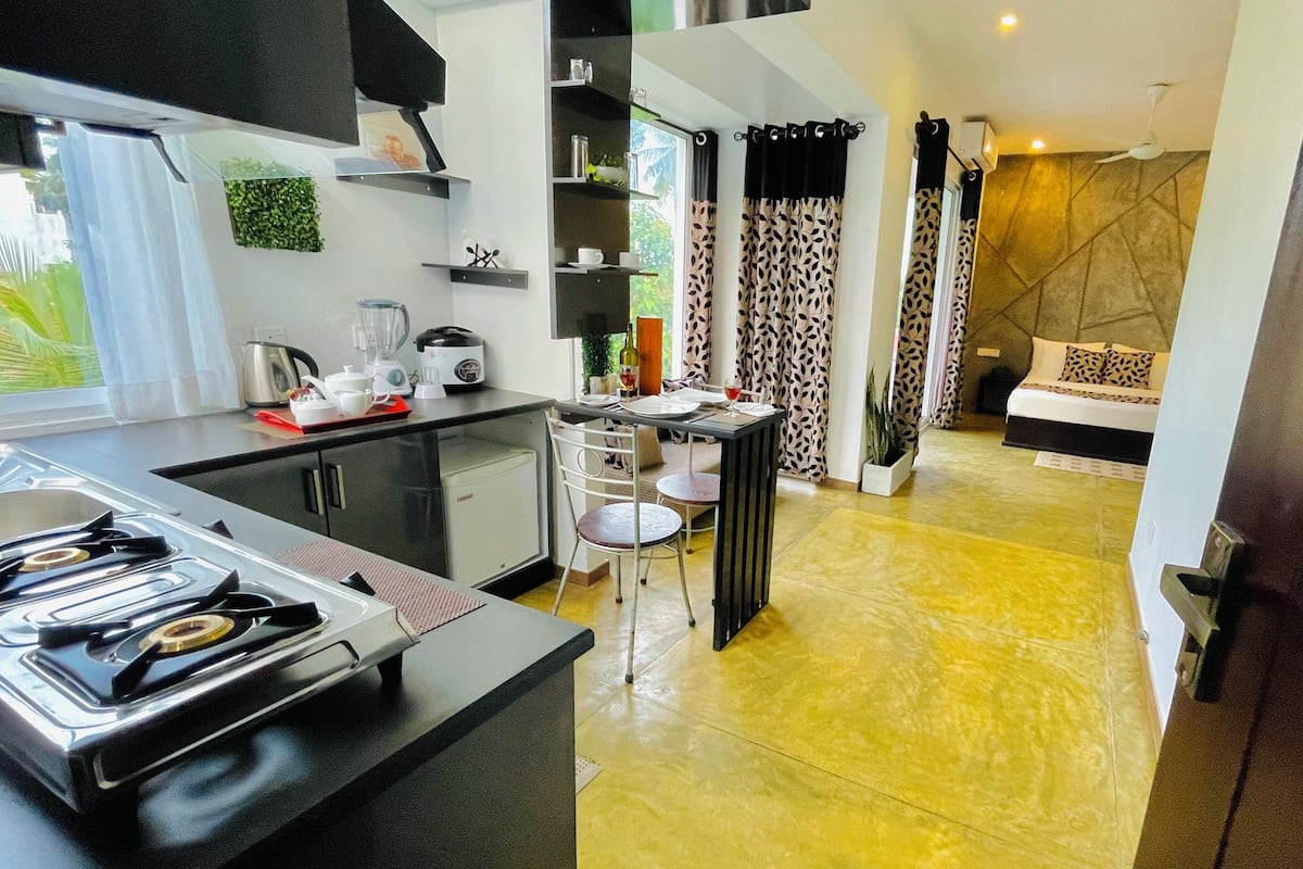 Una cocina moderna con estufa a gas, comedor con mesa y sillas, sala de estar con sofá, y dormitorio con cama.