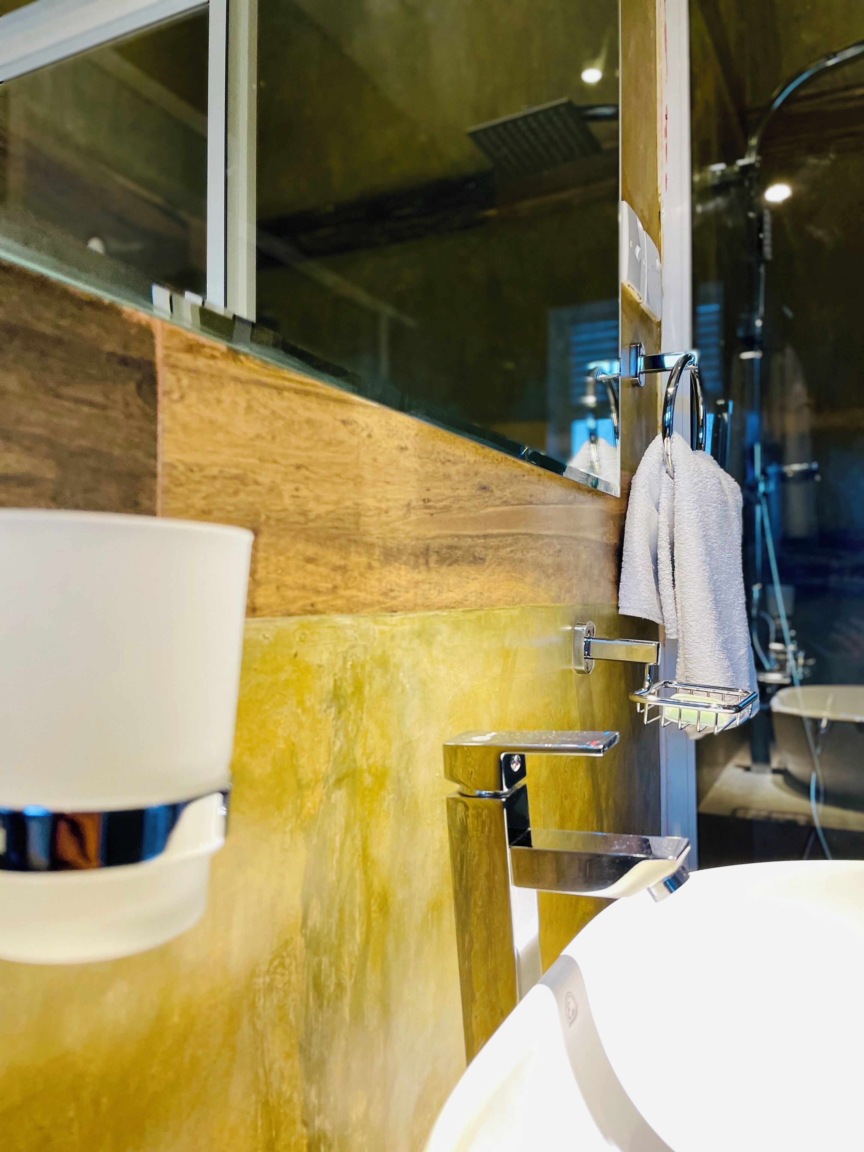 A bathroom with a wooden accent wall, a white sink, a mirror, and a towel rack.