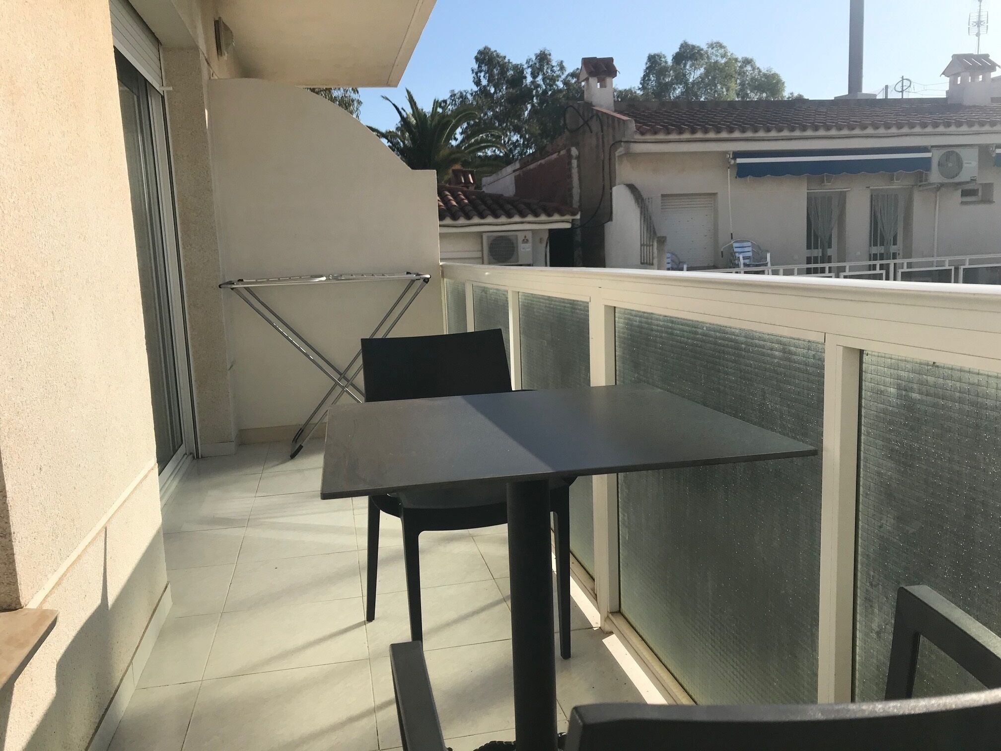 Un balcón con mesa y sillas, un tendedero y vistas del barrio.
