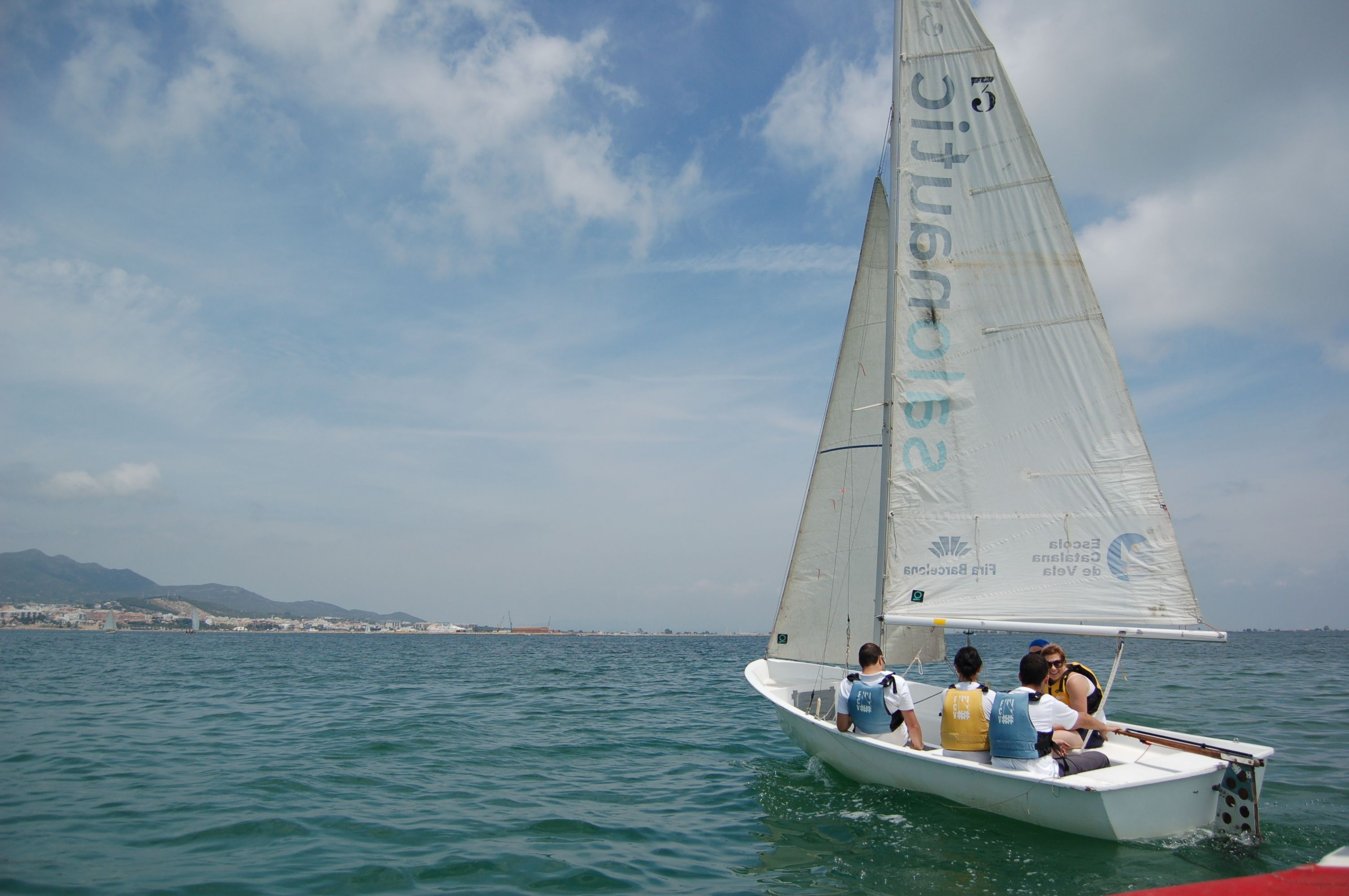 Un voilier transportant des passagers sur une mer calme, avec une terre lointaine et des montagnes en arrière-plan.