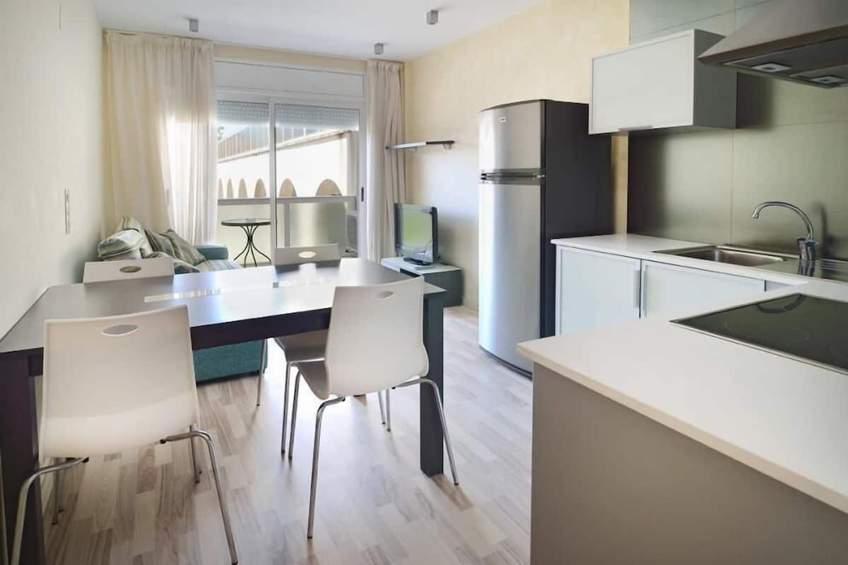 A modern kitchen with a dining area, a refrigerator, a sink, and a window with curtains.