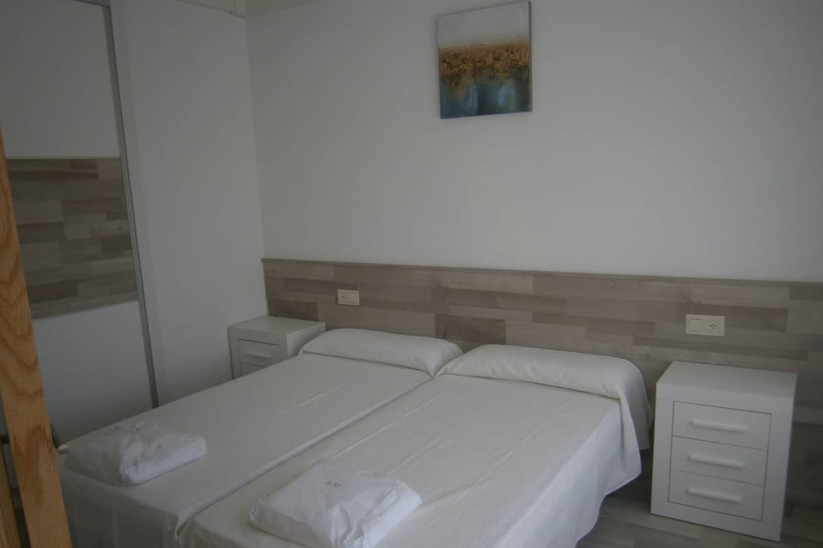 A hotel room with two single beds, a nightstand, a drawer unit, and a painting on the wall.