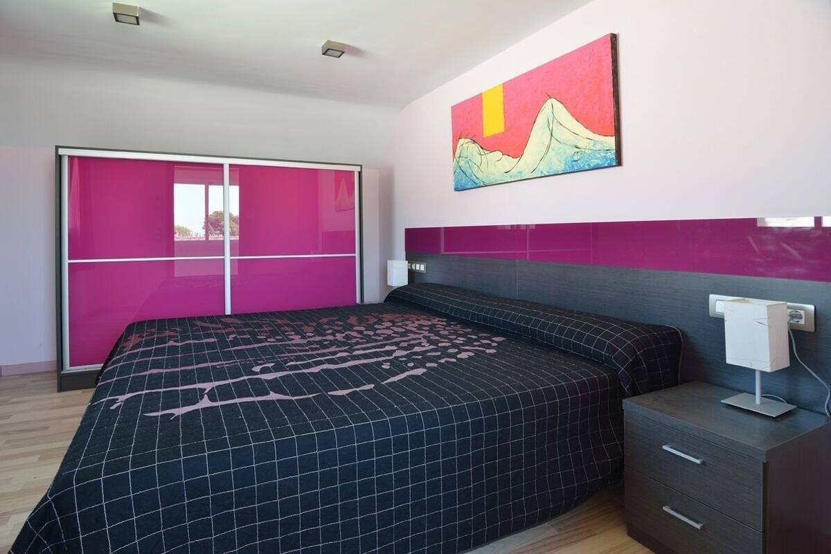 A modern bedroom with a bed, a nightstand, a painting, and a sliding door.