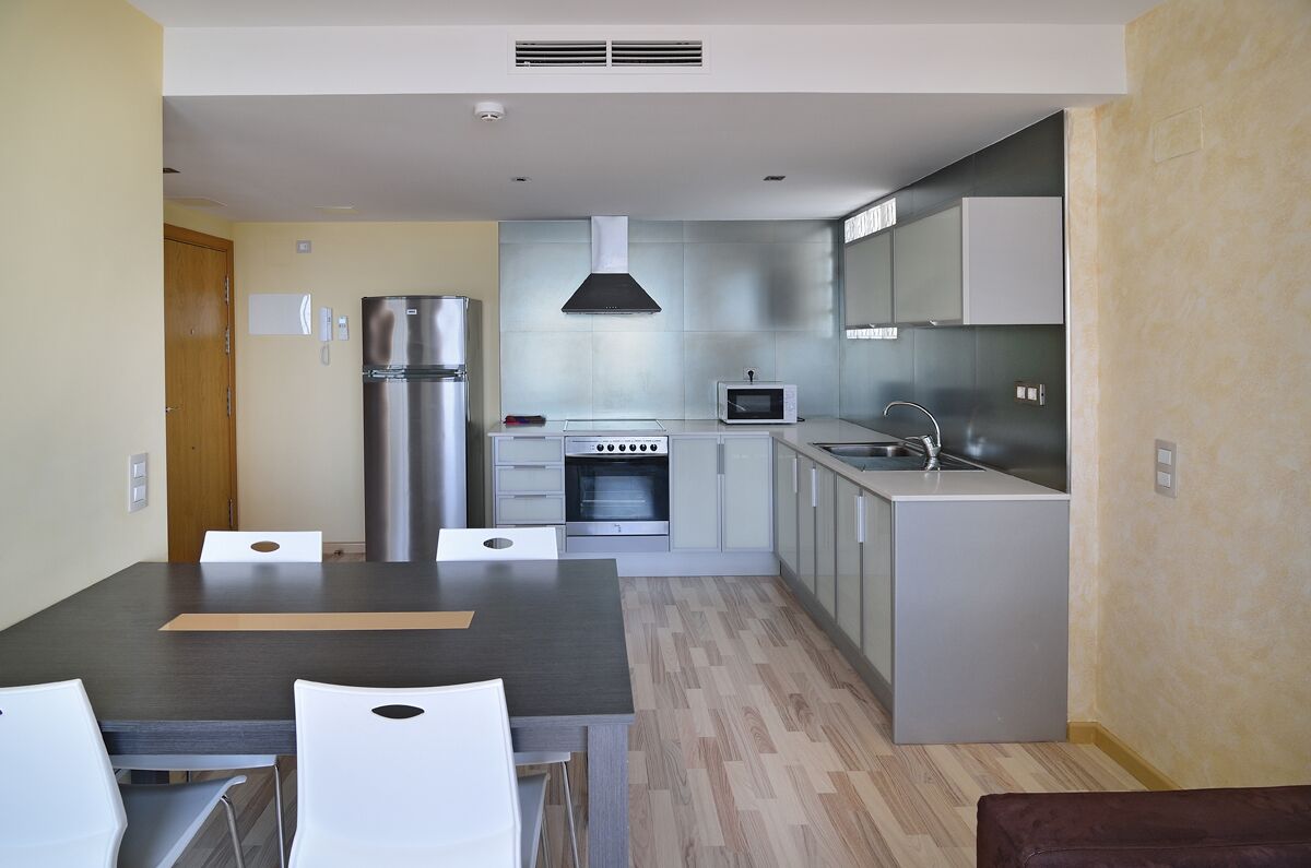 A modern kitchen with stainless steel appliances, a dining area with a table and chairs, and a wooden floor.