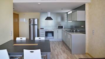 A modern kitchen with stainless steel appliances, a dining area with a table and chairs, and a wooden floor.