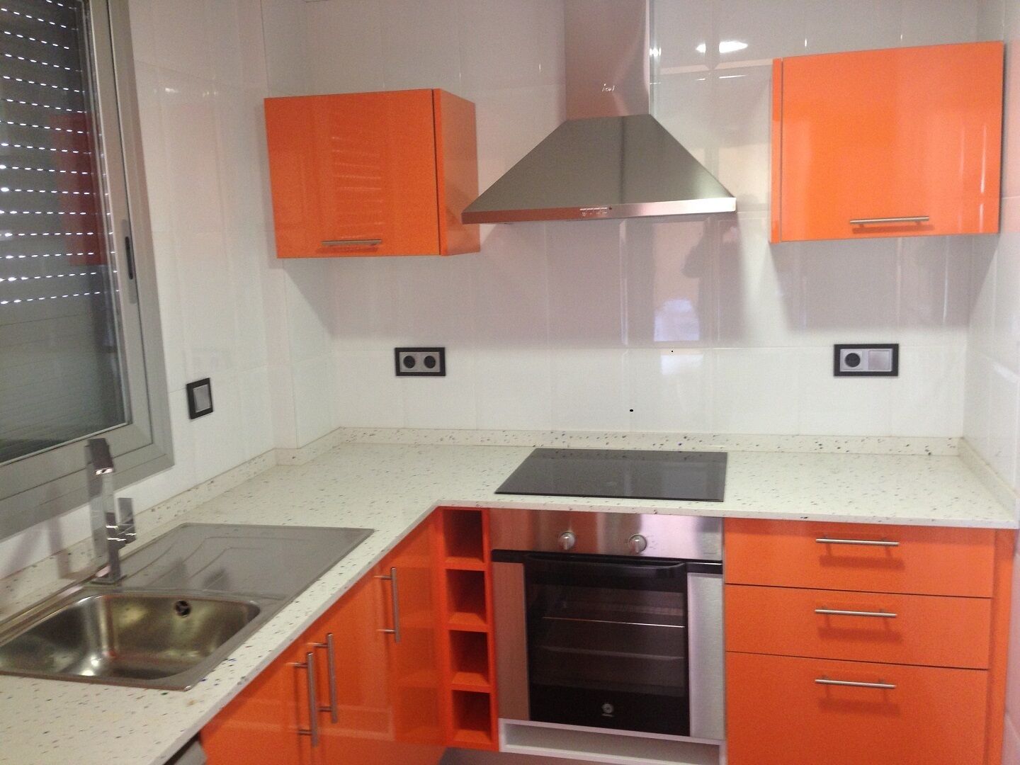 Une cuisine avec des meubles de couleur orange, un évier en acier inoxydable et un four encastré.