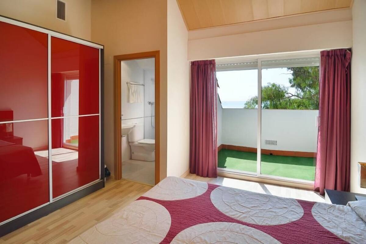 A bedroom with a large sliding door, a bed with a patterned bedspread, a shower area, and a view of a green lawn through a sliding glass door.