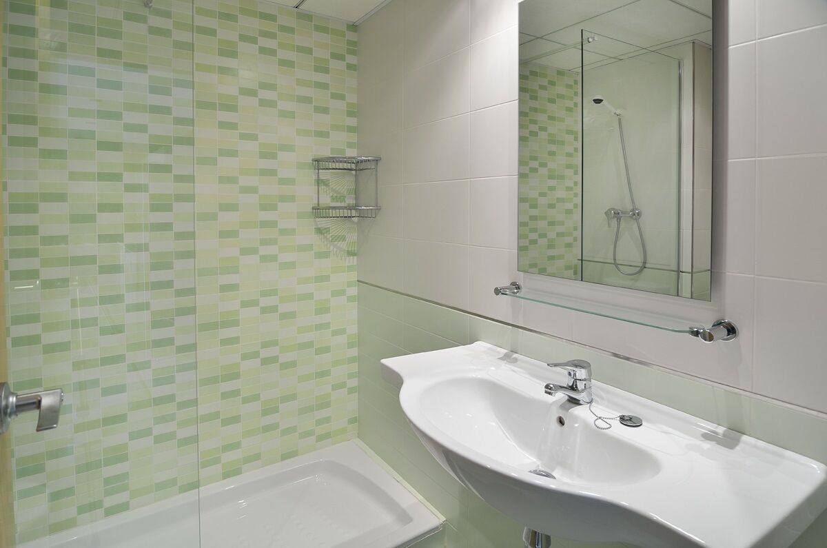 A bathroom with a glass shower enclosure, a white sink, and a tiled wall with a green and white pattern.
