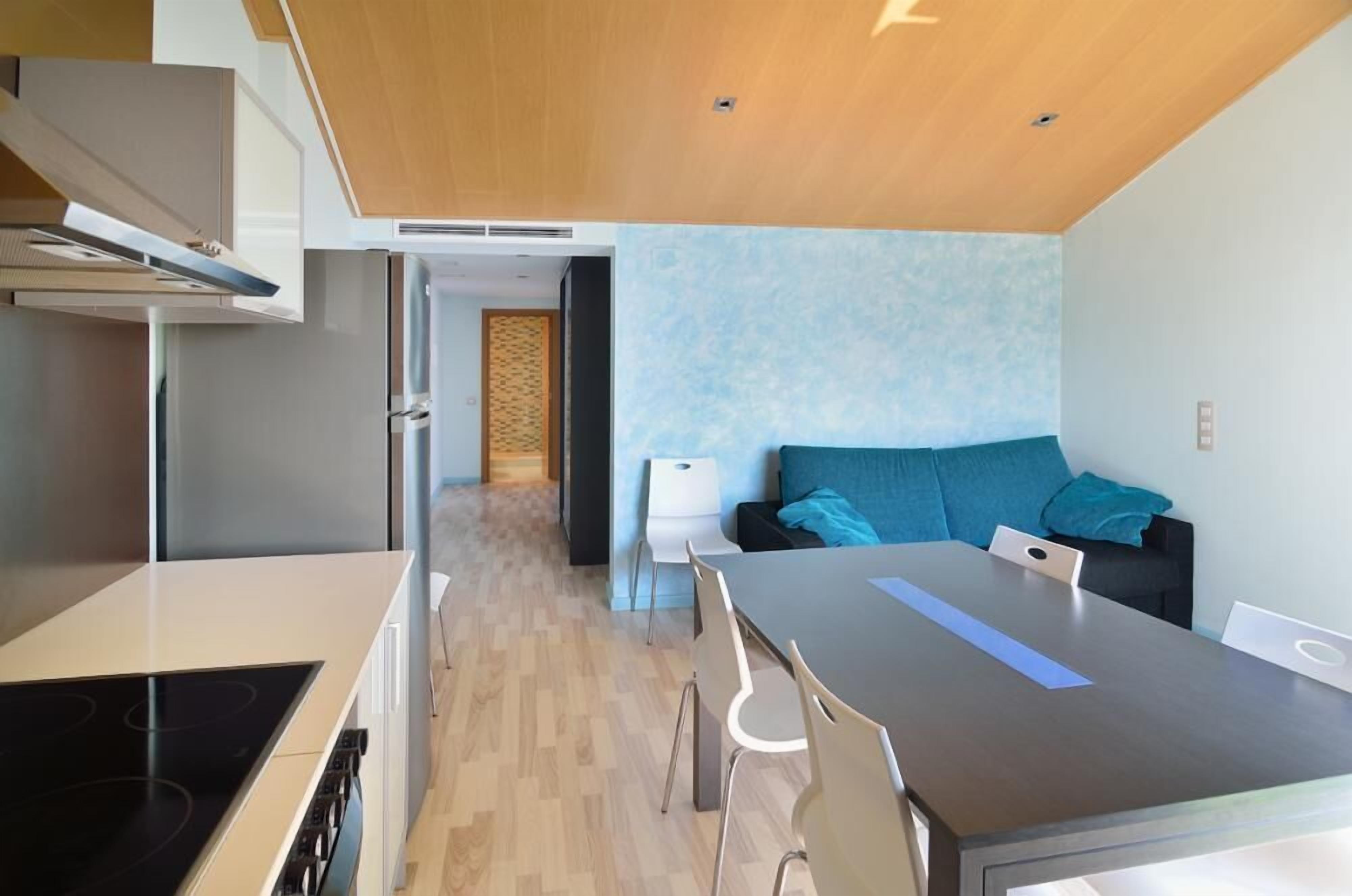 Eine moderne Küche mit Kochinsel, ein Essbereich mit Tisch und Stühlen sowie ein Wohnbereich mit Sofa und Kissen.