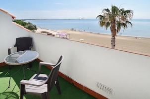 Uma varanda com mesa e cadeiras de vidro, uma palmeira e vista para a praia e o mar.