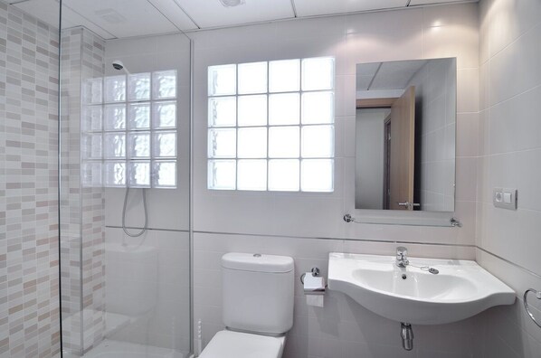 Un baño moderno con cabina de ducha de vidrio, inodoro, lavabo y un espejo grande.