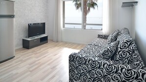 A modern living room with a flat-screen TV, a sofa, and a large window with a view of the sea. - Apartamentos Ornis (Sant Carles de la Rapita)