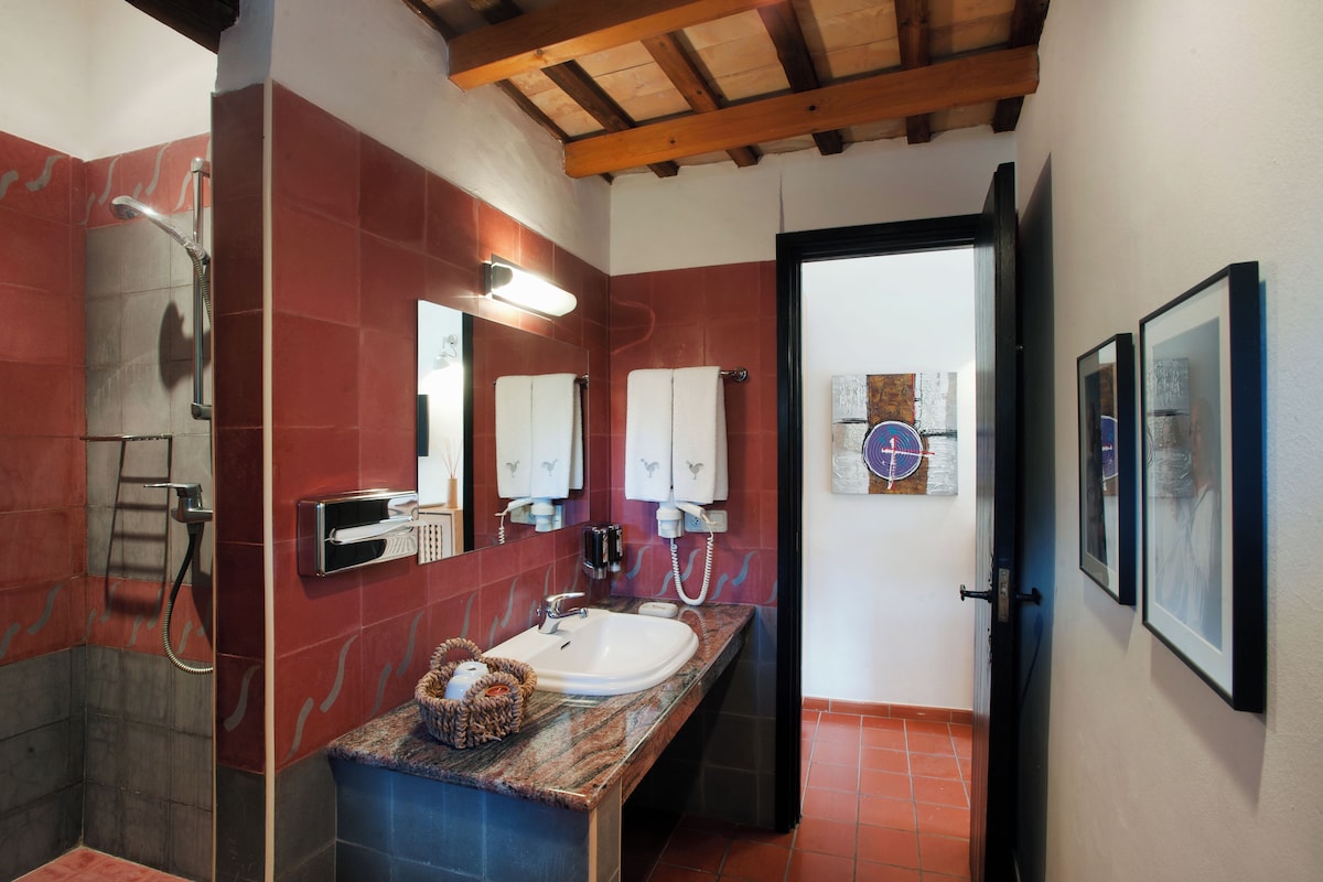 A bathroom with a shower, a sink, and a mirror. There are towels hanging on a rack and a framed picture on the wall.