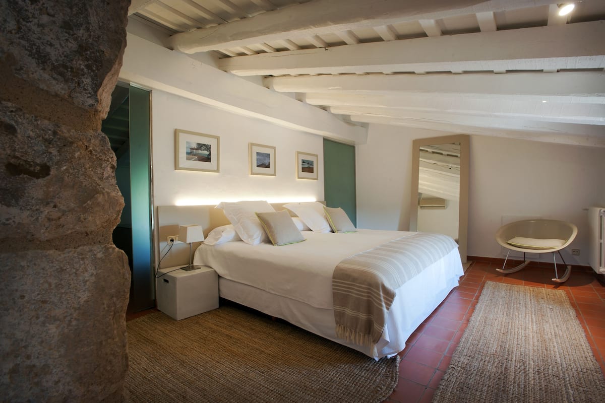 Une chambre avec un grand lit, un fauteuil à bascule et un mur en pierre.