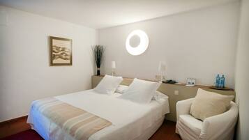 A neatly made bed with white linens, a bedside lamp, and a small table with toiletries.