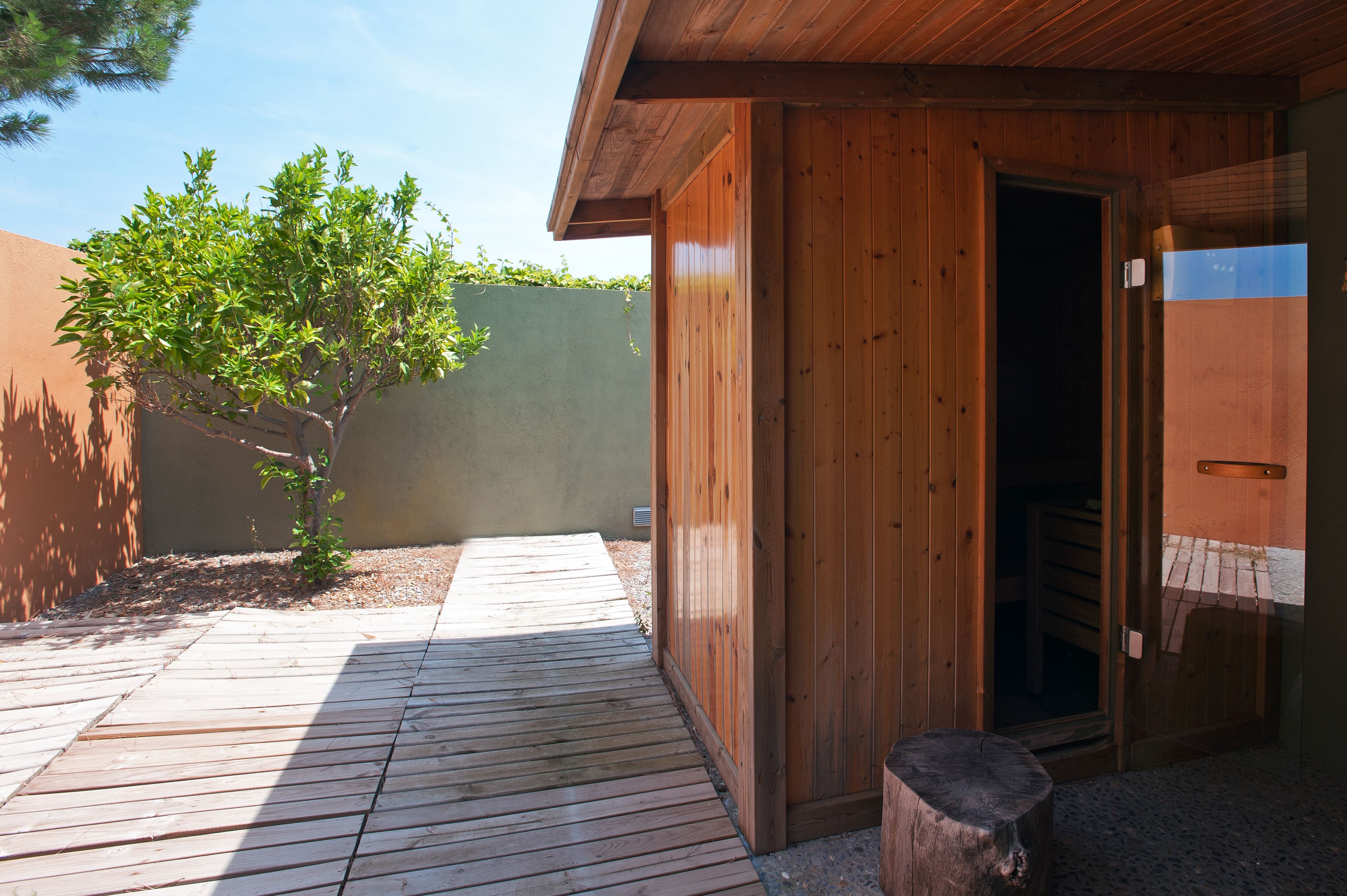 A wooden building with a door open, a small tree, and a wooden deck.