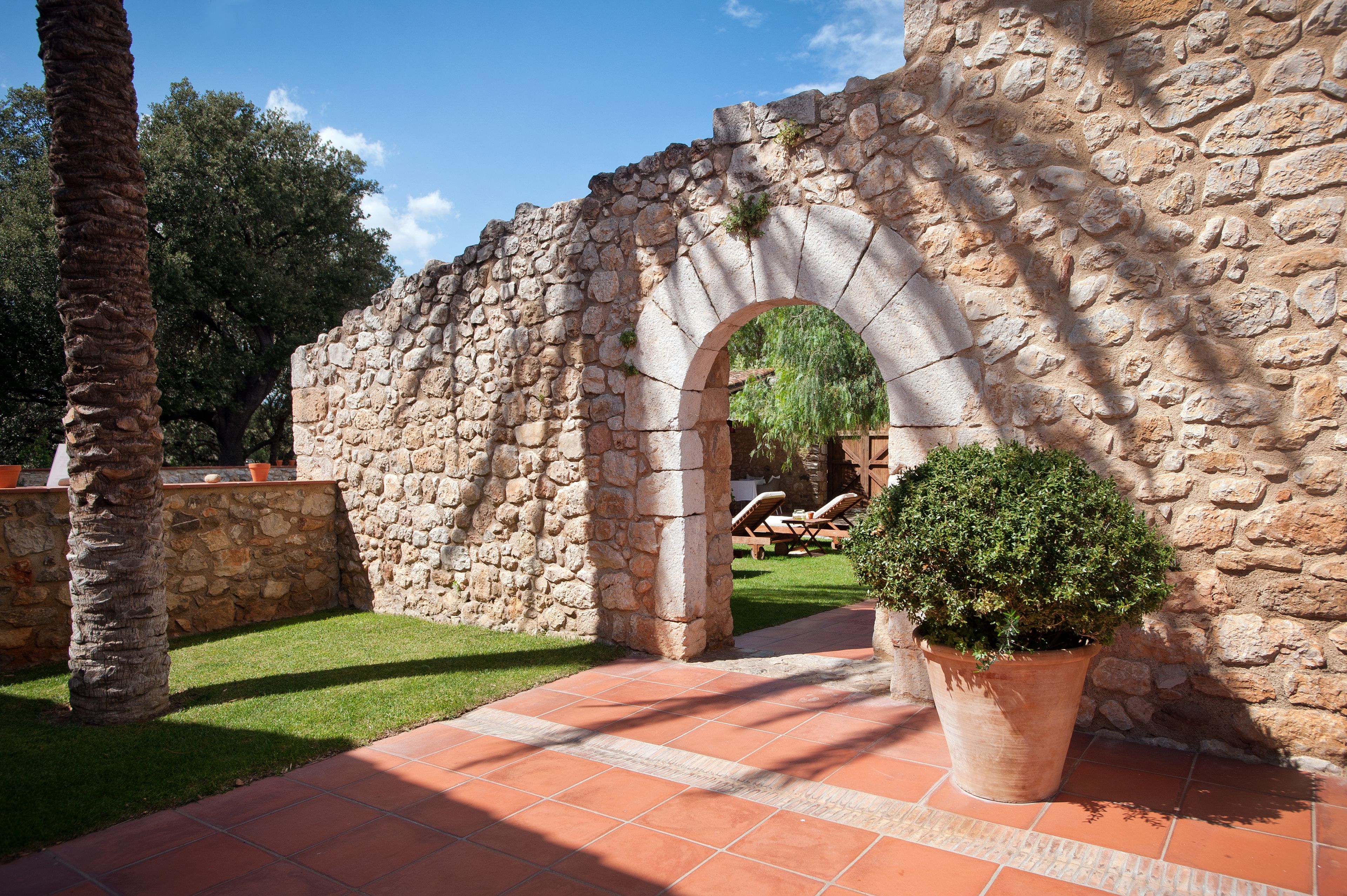 An outdoor stone archway with a potted plant in the foreground.