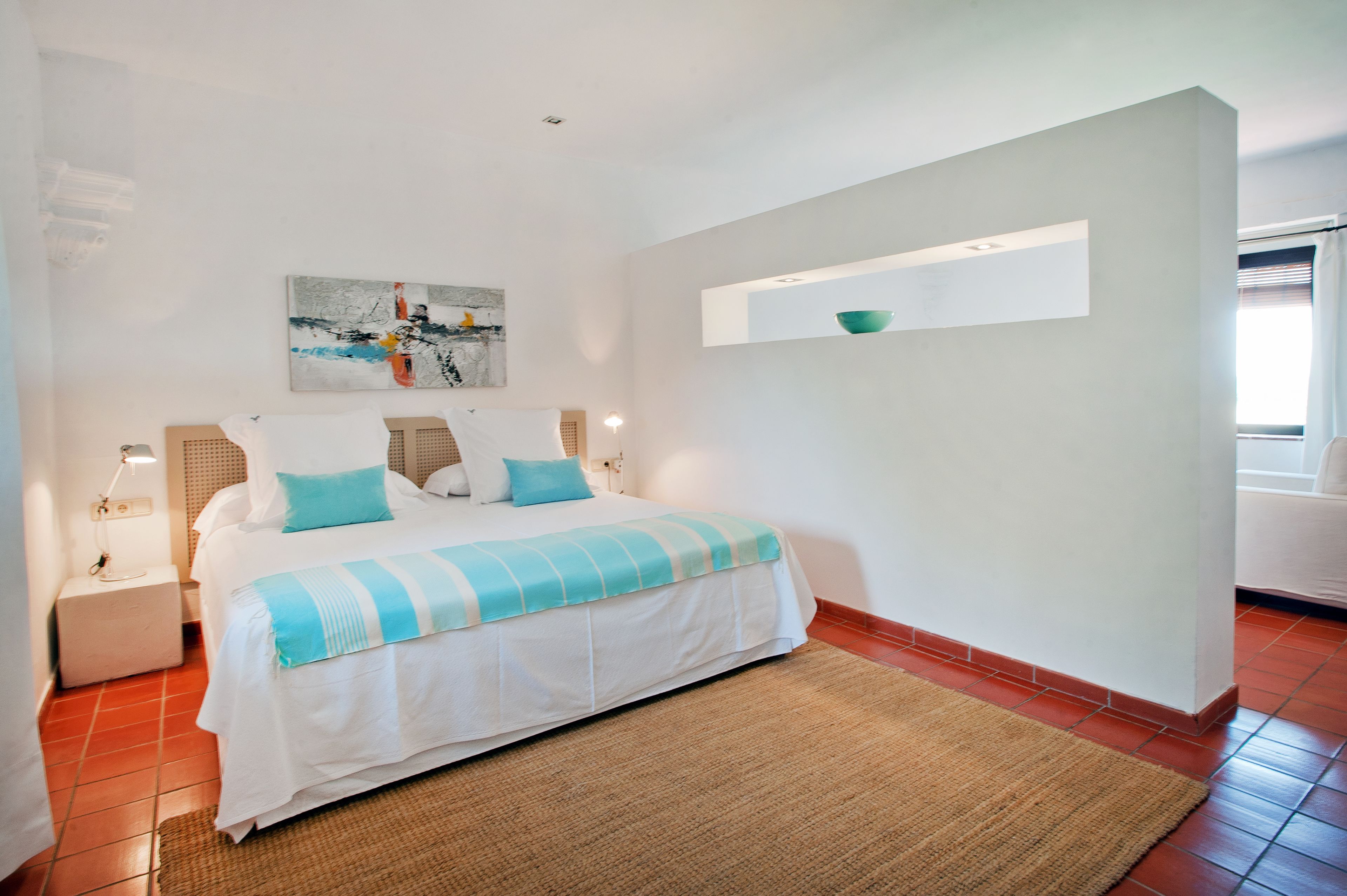 Un dormitorio con cama, mesita de noche, estante en la pared y ventana.