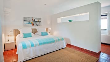 Un dormitorio con cama, mesita de noche, estante en la pared y ventana.