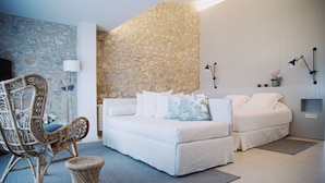 A modern living room with a stone accent wall, a white sofa, a wicker chair, and a small side table. - Mas Falgarona Hotel Boutique and Spa (Avinyonet de Puigventos)