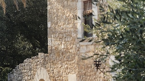 A stone building with an arched doorway, a sofa with red cushions, and potted plants. - Mas Falgarona Hotel Boutique and Spa (Avinyonet de Puigventos)