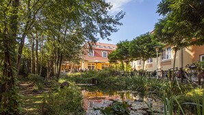 A courtyard with a pond, surrounded by trees and buildings. - Hotel Zum Leineweber (Burg (Spreewald))