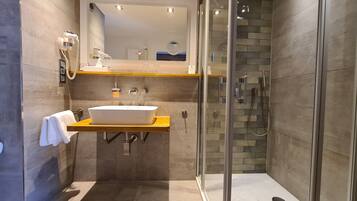 A modern bathroom with a glass-enclosed shower, a wooden vanity with a white sink, and a towel hanging on the wall.