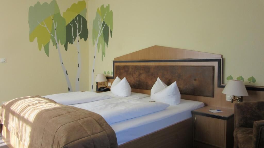 A hotel room with a large bed, a wooden headboard, two bedside tables with lamps, and a wall mural of trees.