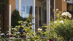 A house with a glass door entrance, a tiled roof, and a garden with various flowers. - Hotel Zum Leineweber (Burg (Spreewald))