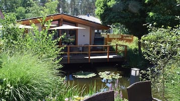 A house with a deck over a pond, surrounded by lush greenery.