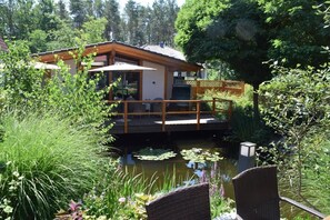Una casa con terraza sobre un estanque, rodeada de exuberante vegetación.