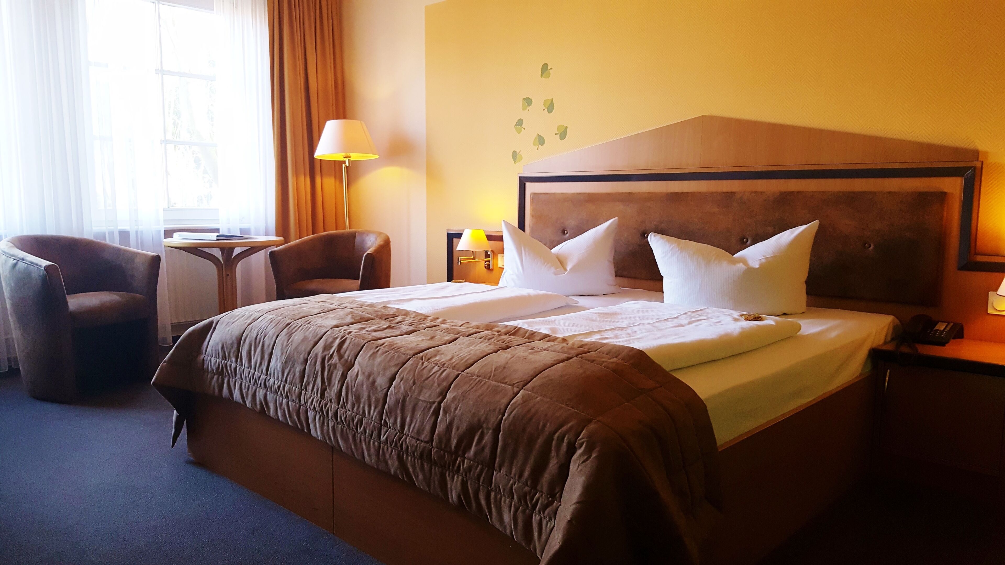 Habitación de hotel con una cama grande, dos sillas, una mesita, una lámpara y un teléfono instalado en la pared.